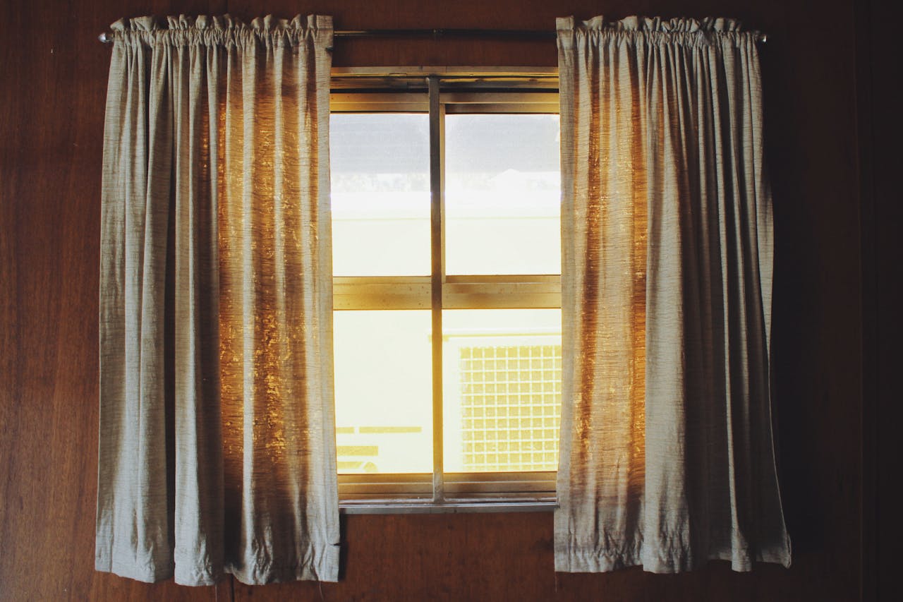 services-01 Warm sunlight streaming through fabric curtains in a wooden interior setting.